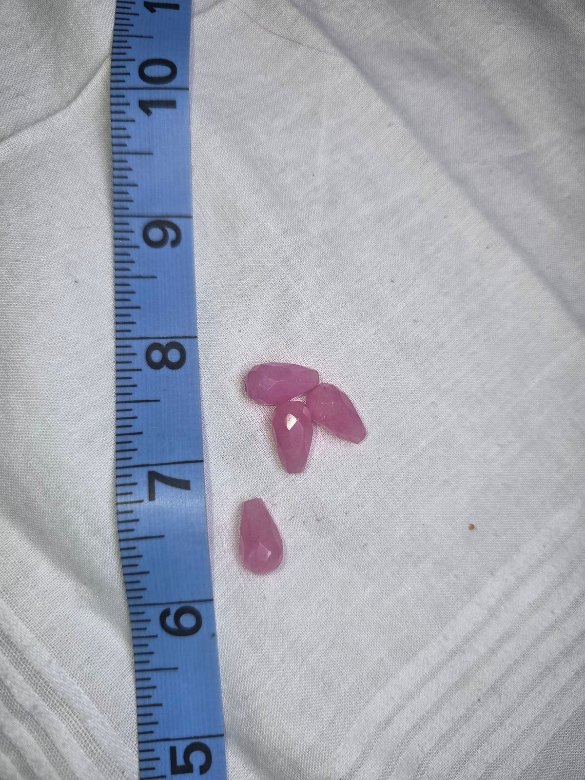 Four light pink faceted teardrop drop beads with ruler for scale