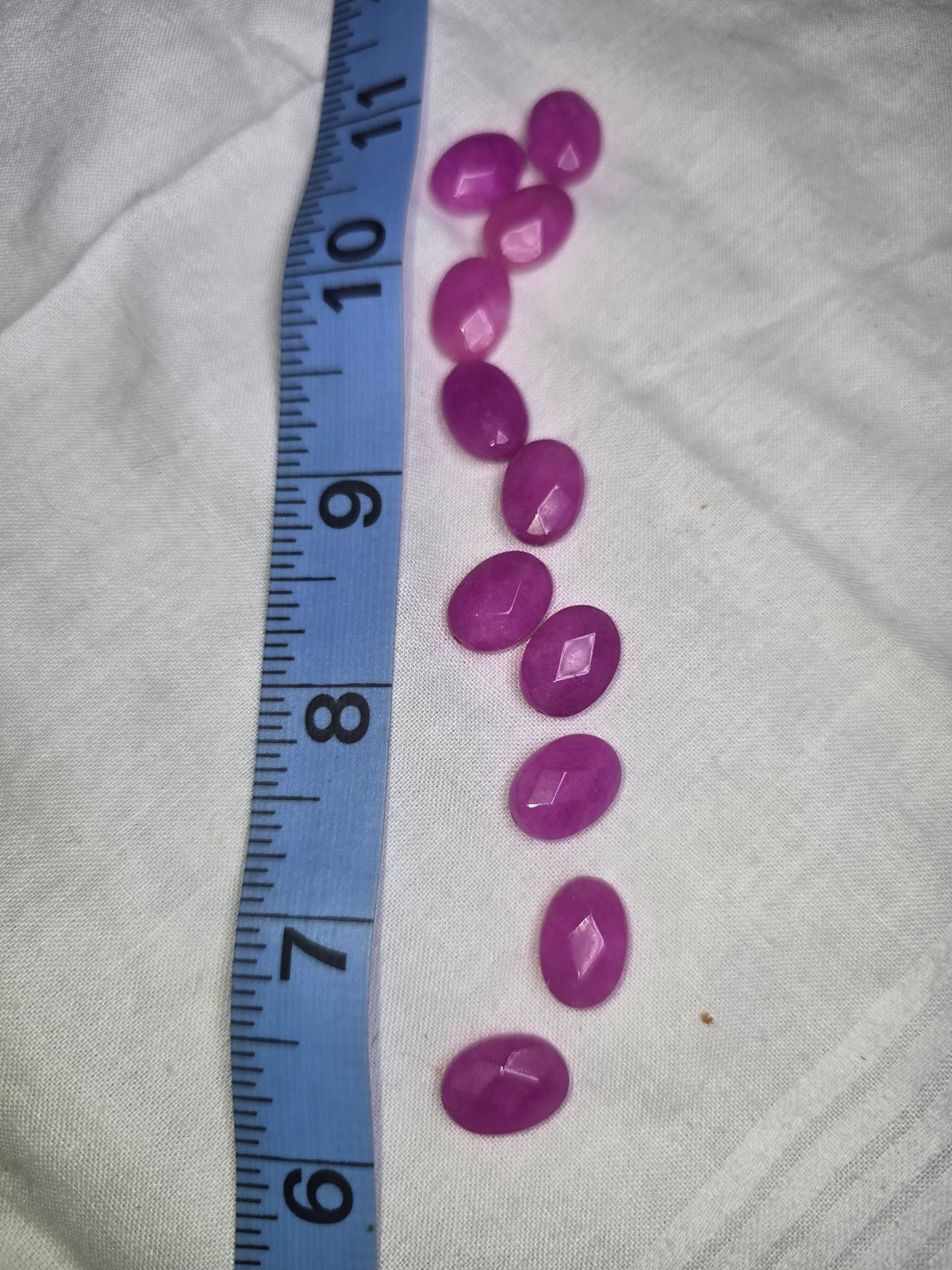 Ten bright magenta-purple faceted oval beads laid out with ruler for scale