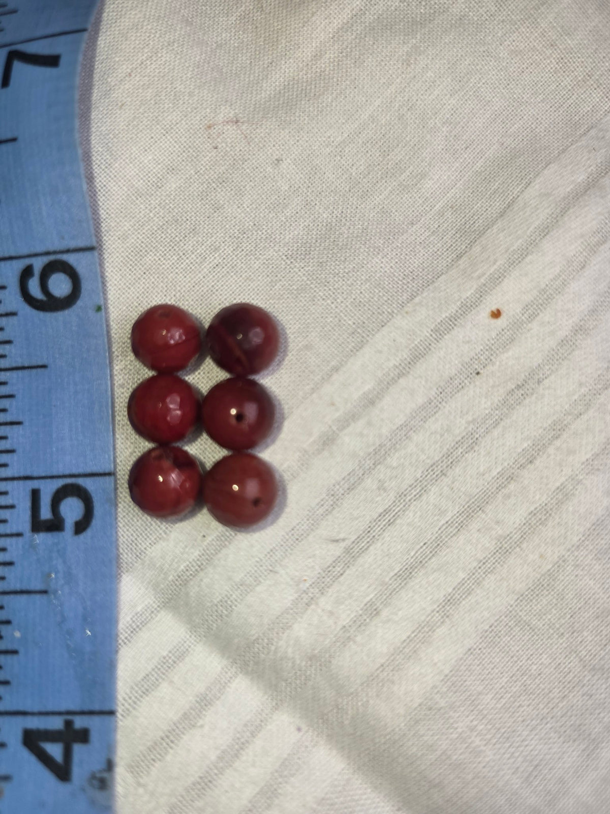 Six deep brick-red round beads with ruler for scale