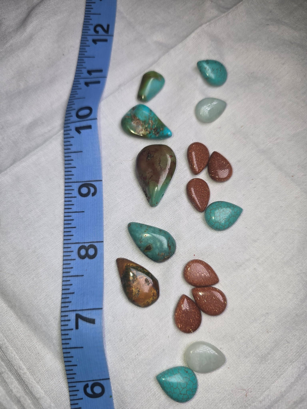 Mixed genuine turquoise, goldstone and pale stone teardrop beads with ruler for scale