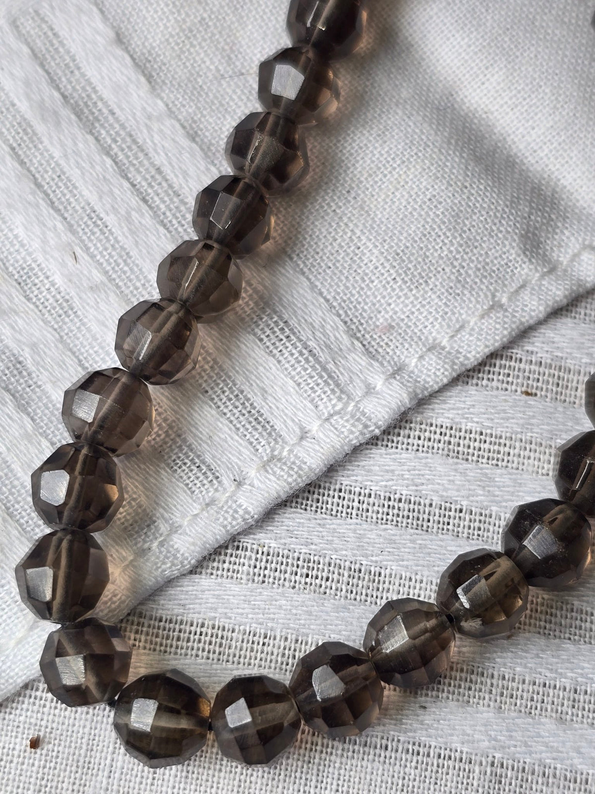 Smoky quartz faceted round bead strand hand closeup