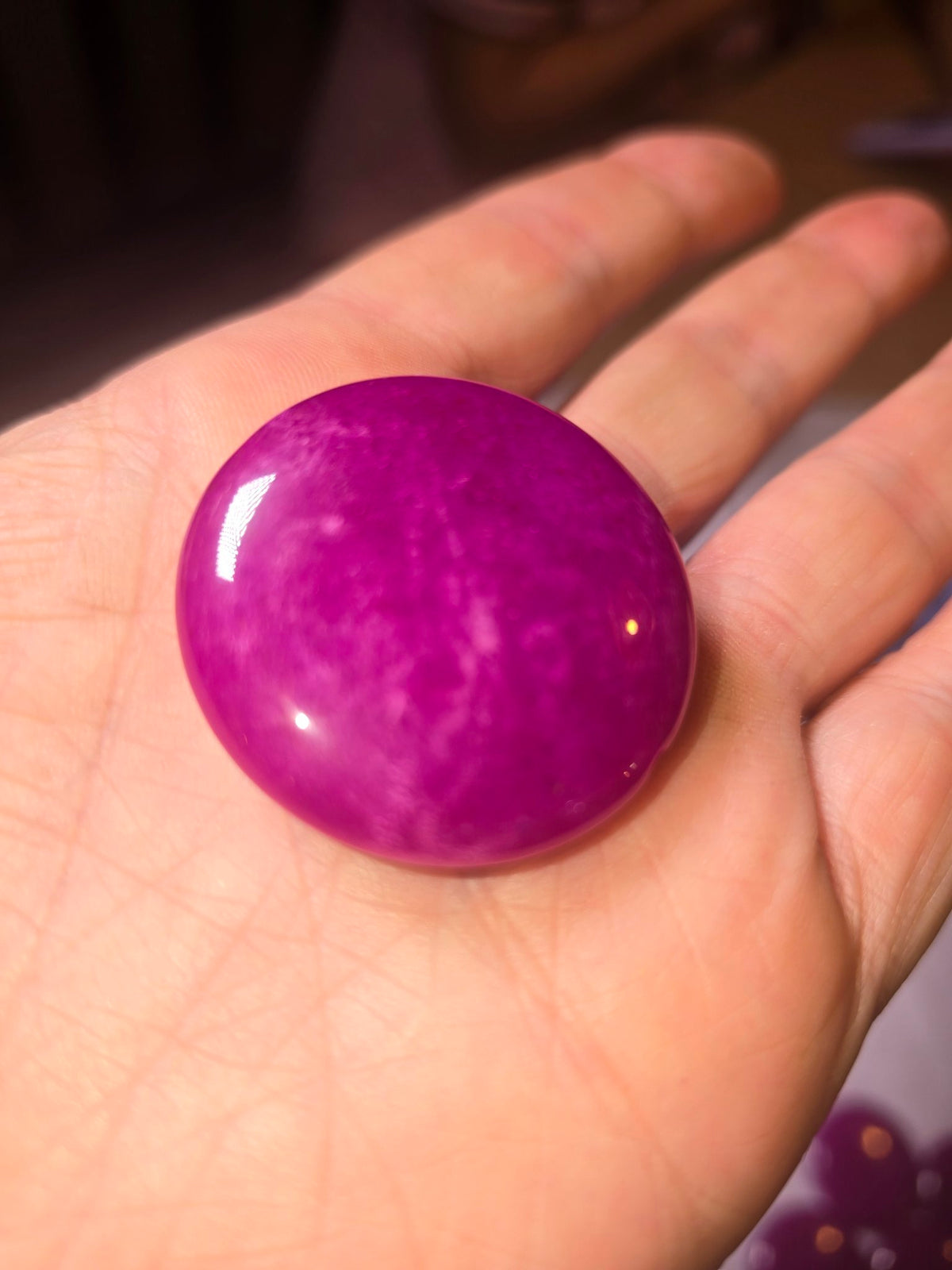 Closeup of one large magenta-purple jade coin bead in hand showing mottled pattern