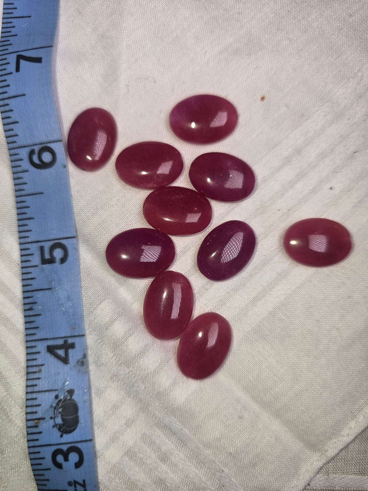 Ten raspberry pink-red flat oval beads with ruler for scale