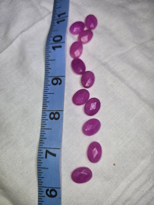 Ten bright magenta-purple faceted oval beads laid out with ruler for scale