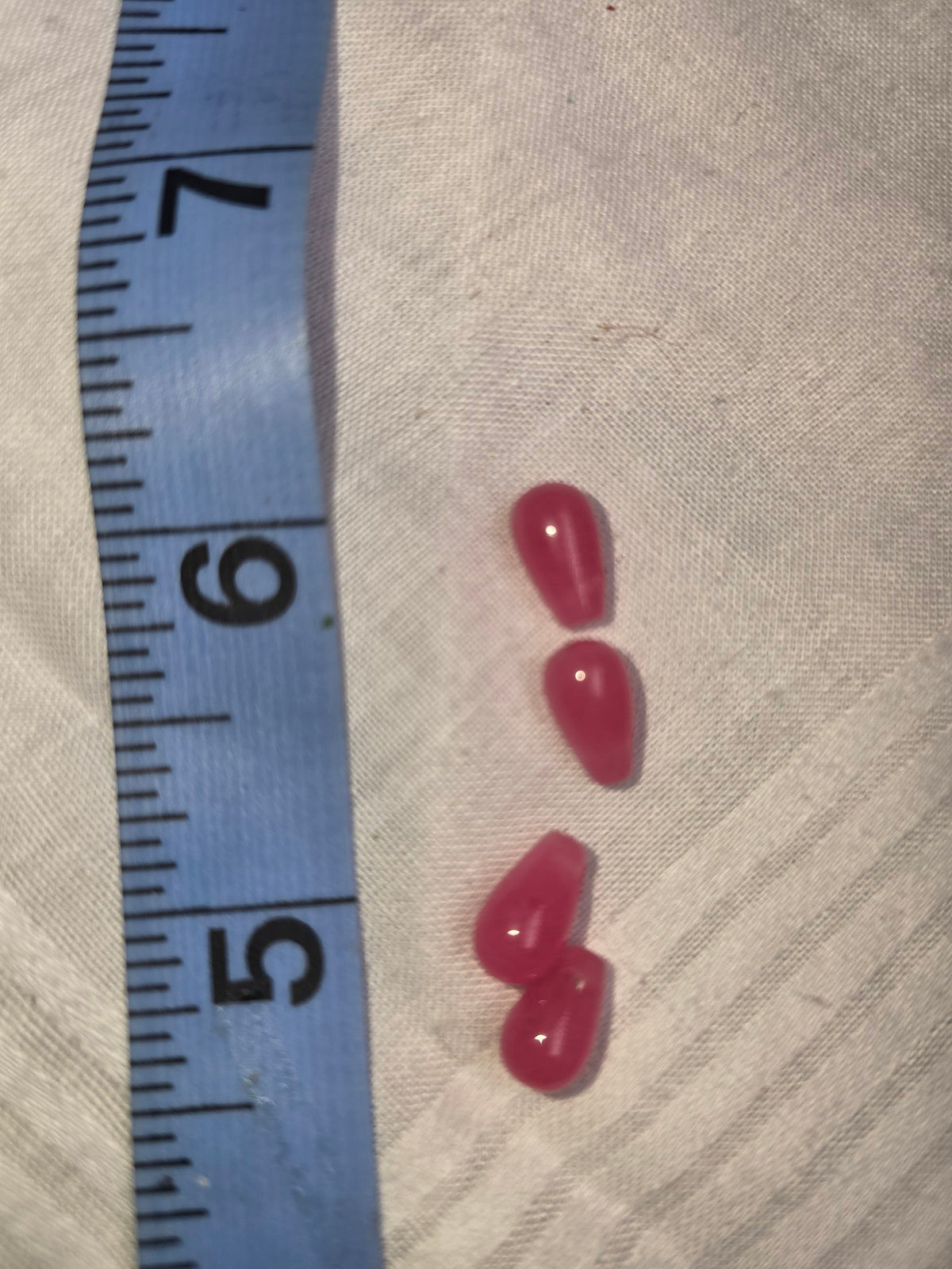 Four pink-red smooth teardrop beads with ruler for scale