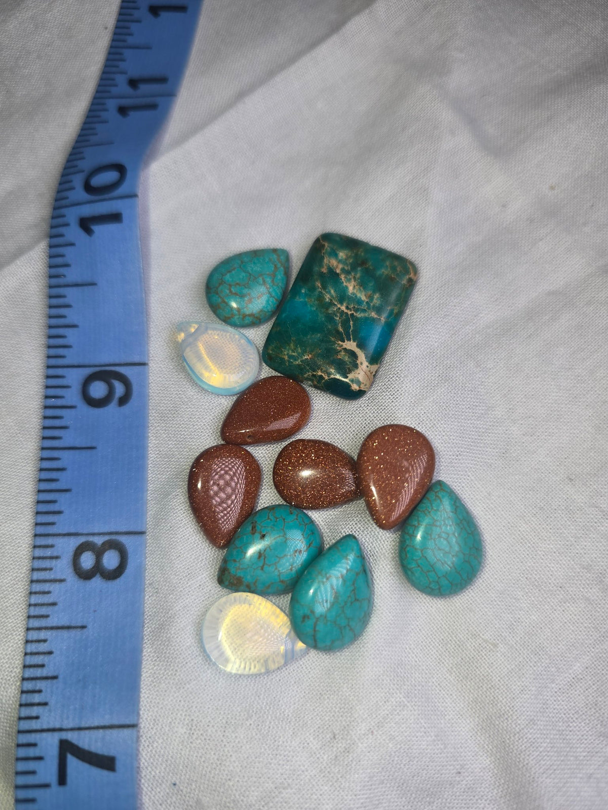 Mixed serpentine turquoise, goldstone and opalite teardrop pieces with ruler for scale