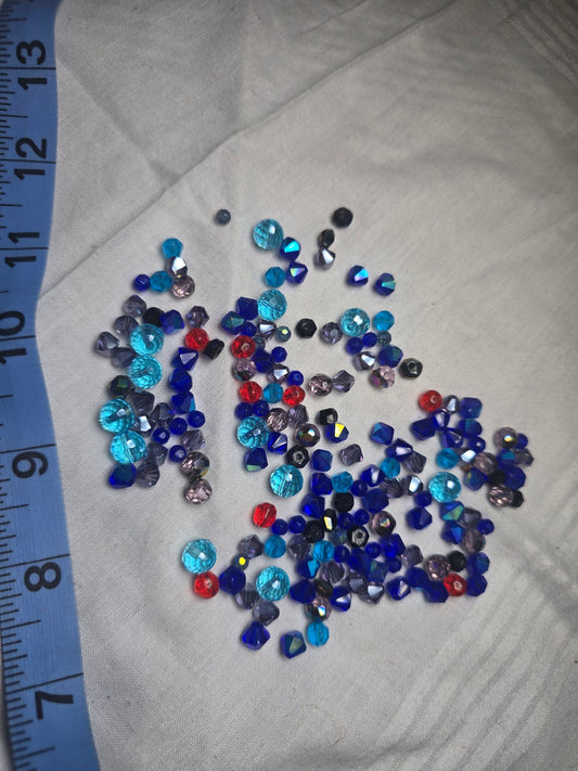 Mixed small crystal bicone beads in blue, aqua, purple, red and black with ruler for scale