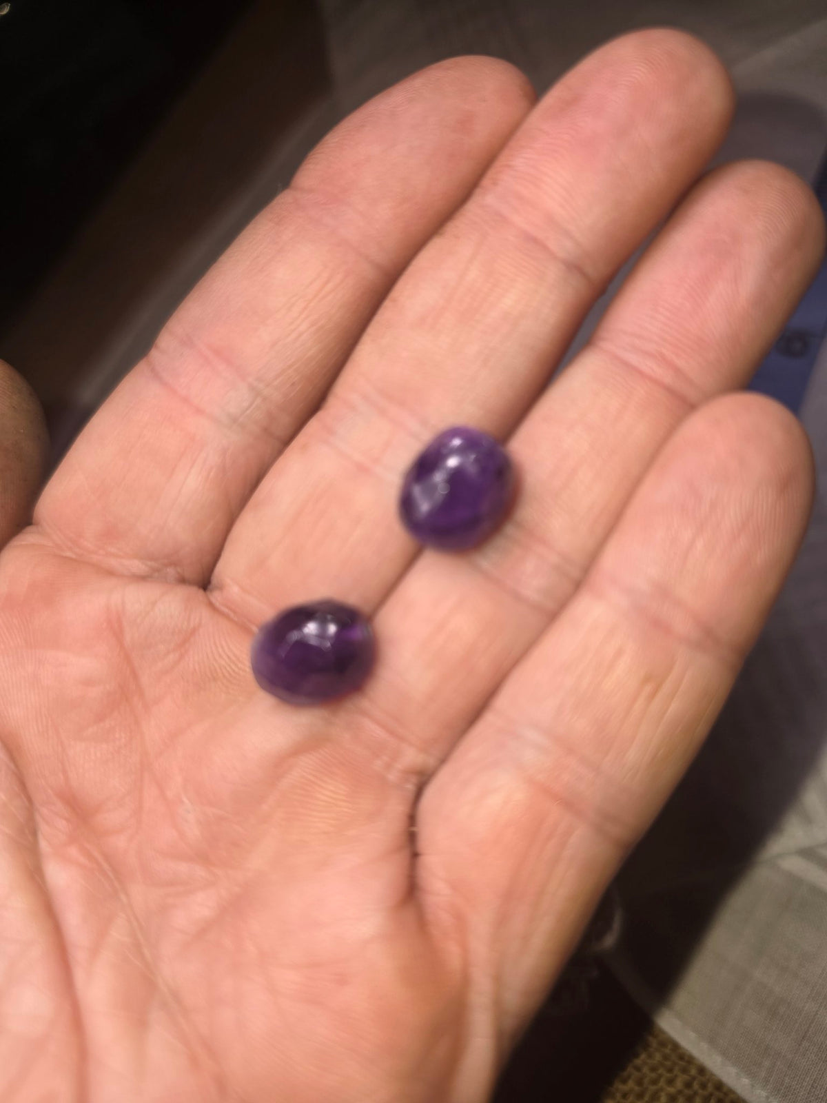 Two deep purple faceted beads held in hand for colour and size