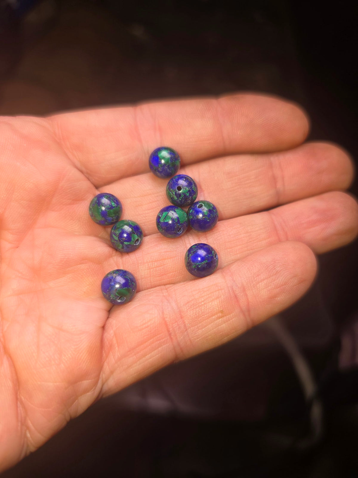 Eight azurite-malachite beads held in hand showing blue and green colour