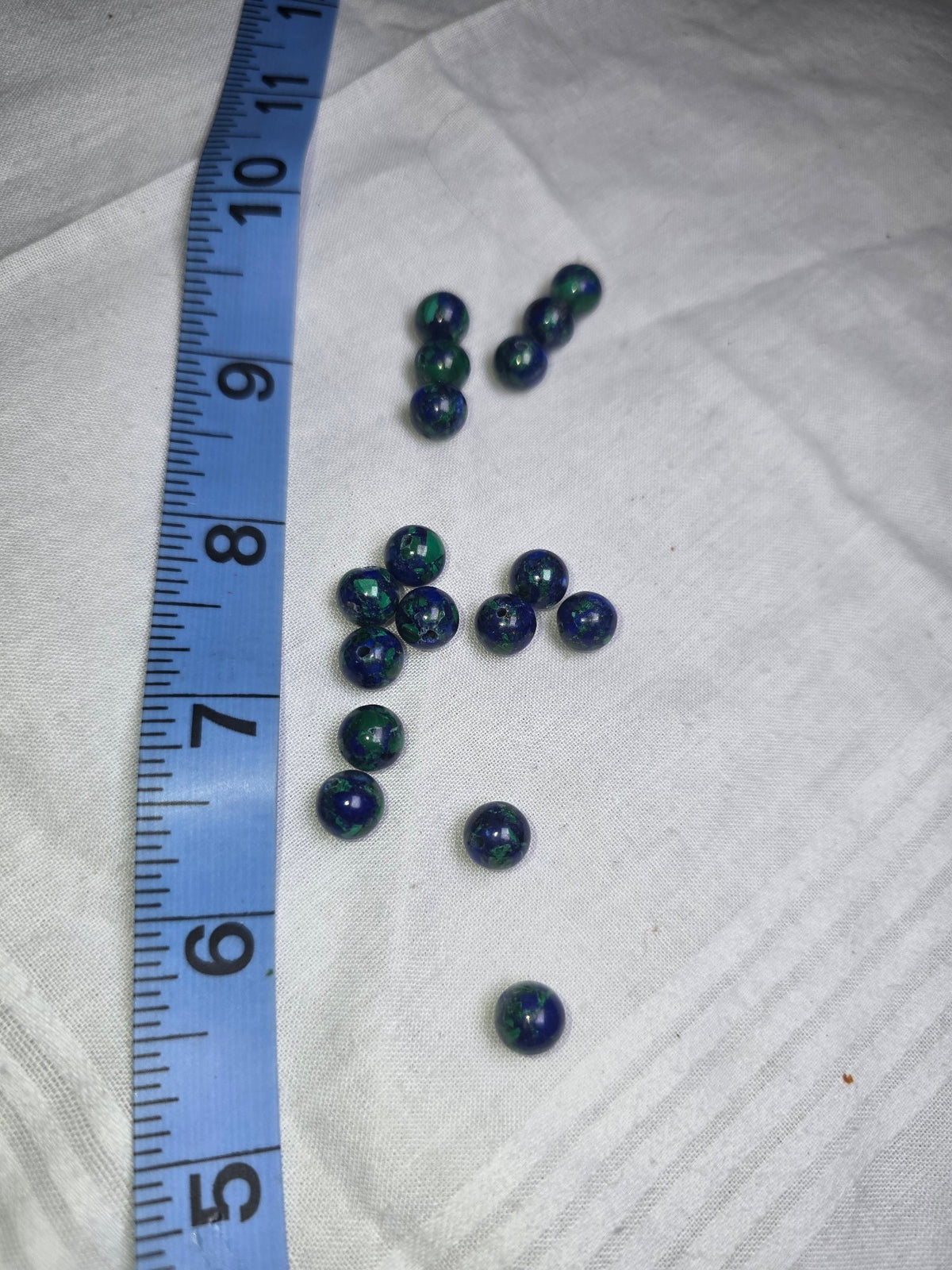 Seventeen blue and green azurite-malachite round beads with ruler for scale