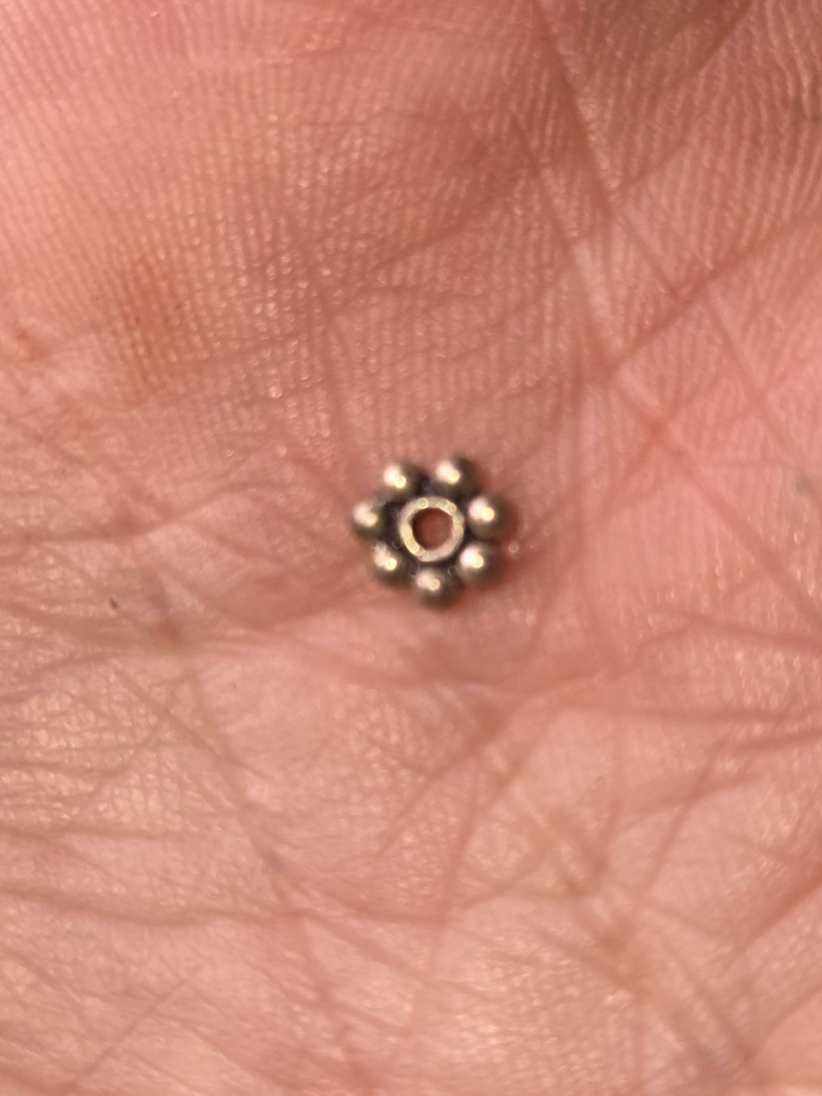 Closeup of one silver flower spacer bead in hand