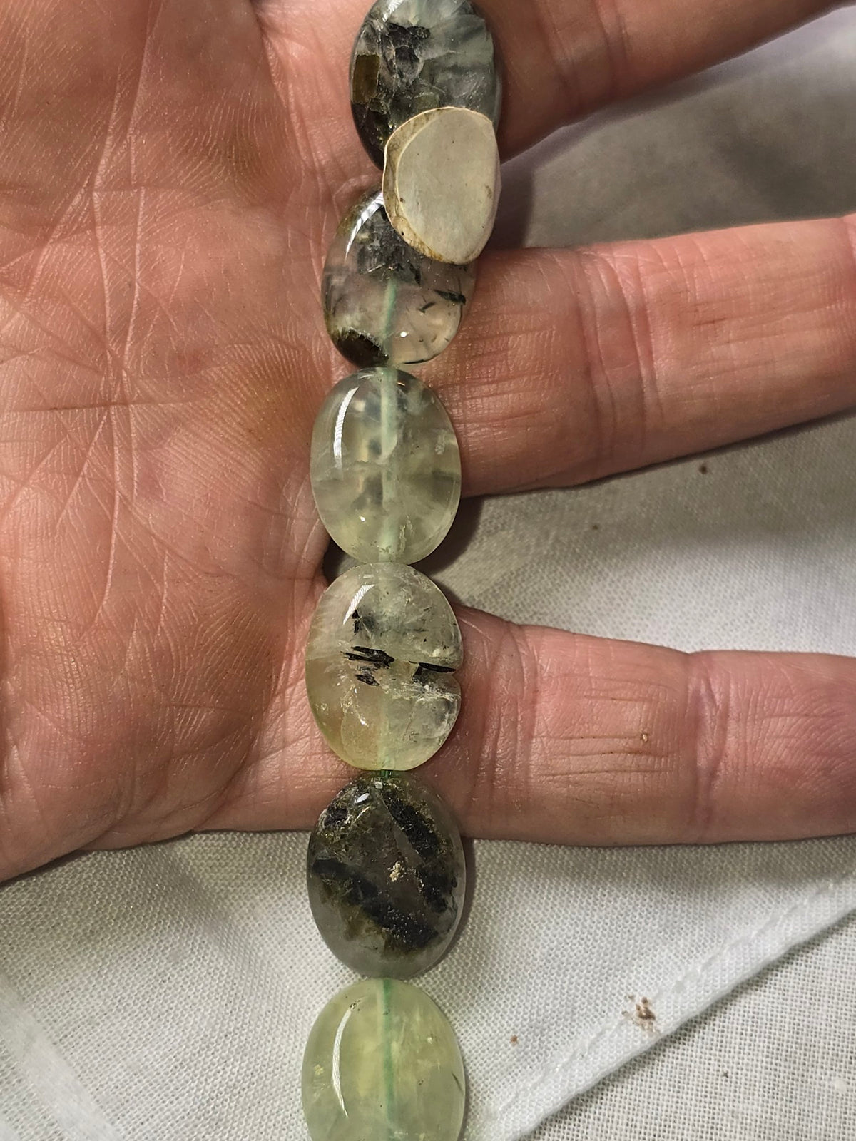 Prehnite oval beads in hand showing inclusions